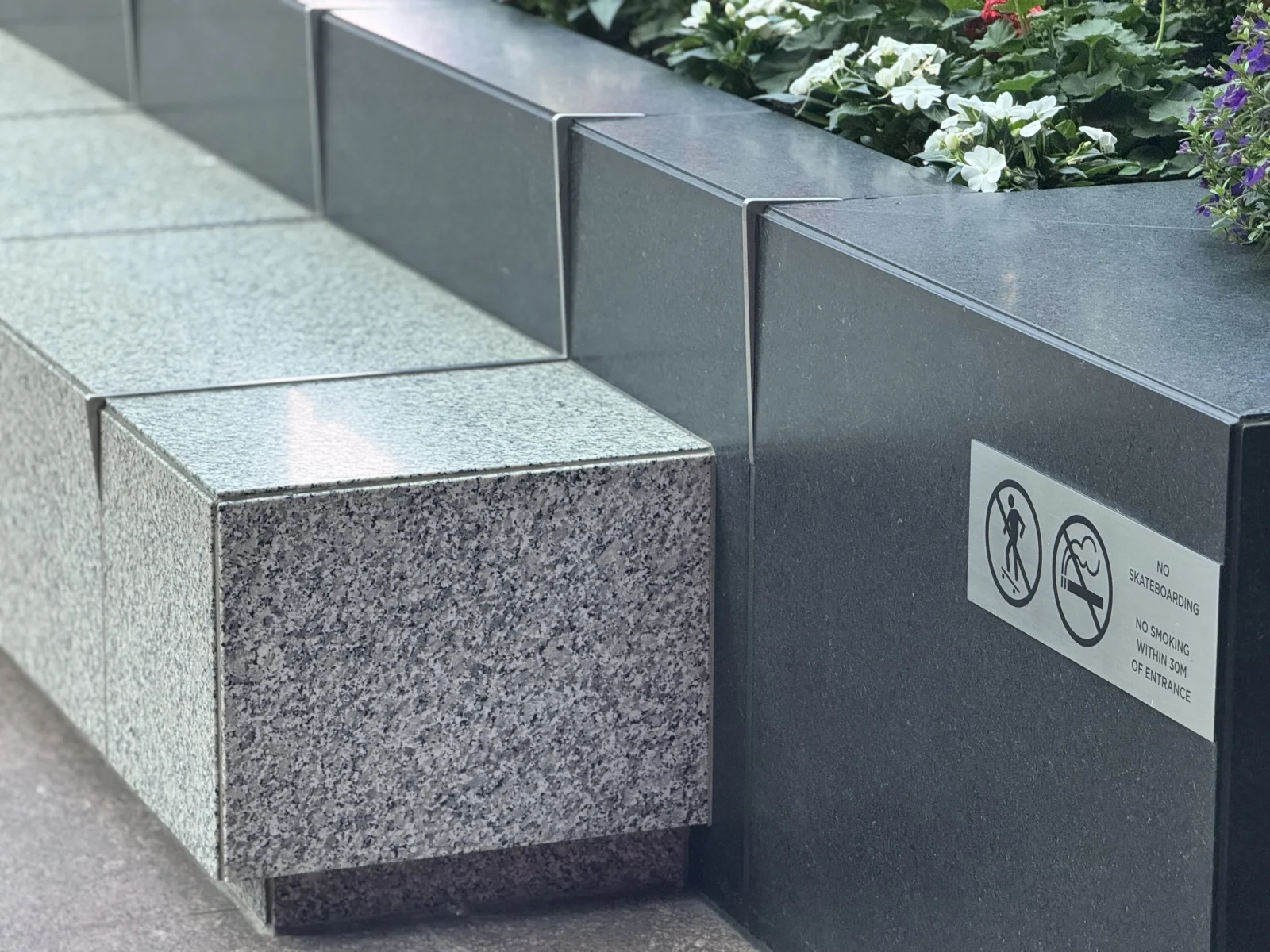 Skate stoppers installed on a granite planter wall with no-skateboarding signage in a Canadian downtown plaza