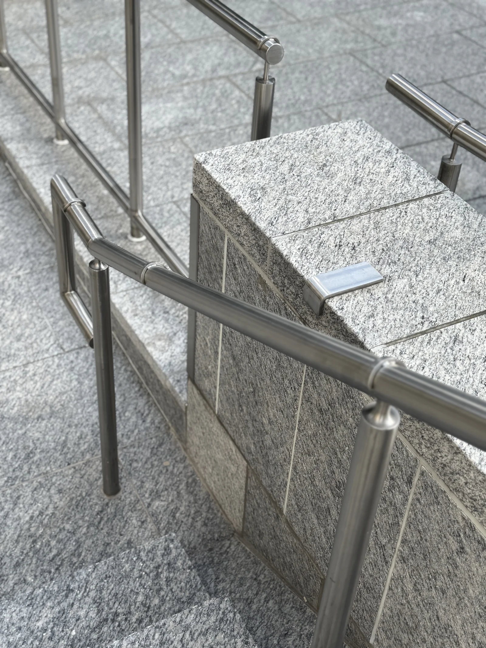 Stainless saddle-stop skateboard deterrents clamped on round handrails along a granite staircase in Canada