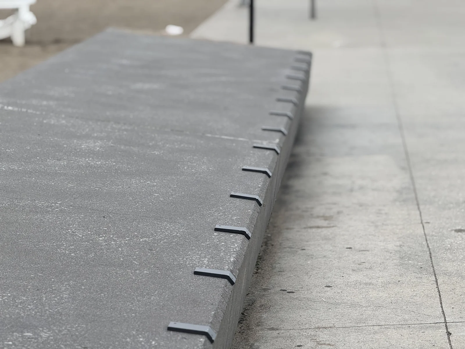 Skateboard deterrents installed along a painted concrete ledge with notched anti-grind edge profile in a Canadian commercial plaza